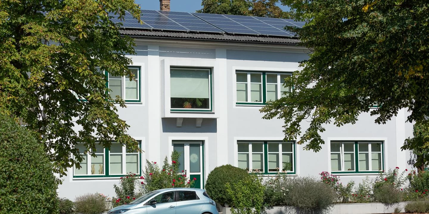 Ein Haus mit einer Solaranlage am Dach und einem Elektroauto vor der Tür. 