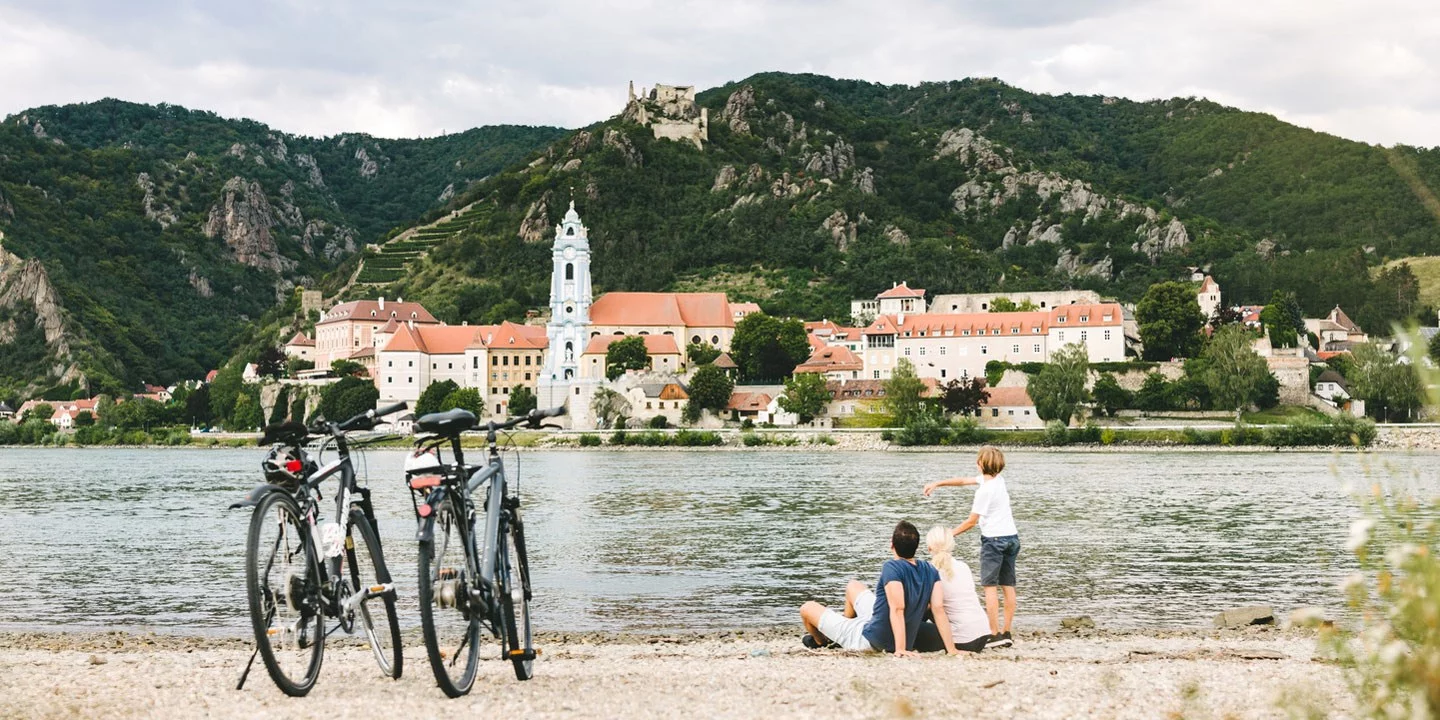 Donauradweg: Eine Familie sitzt am Flussufer und blickt auf Dürnstein.