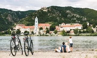 Donauradweg: Eine Familie sitzt am Flussufer und blickt auf Dürnstein.